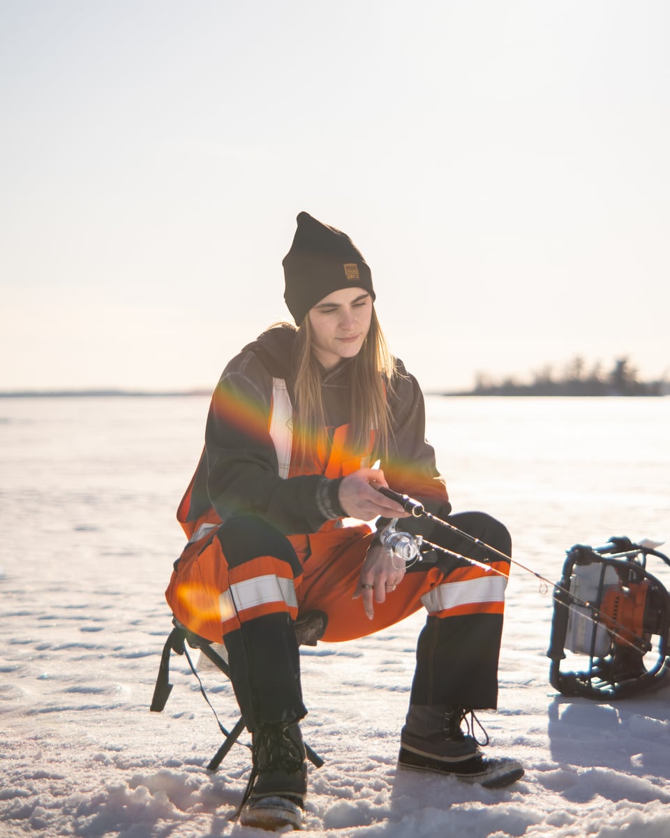 Lifestyle photograph of a worker ice fishing on a frozen Manitoba lake at sunrise