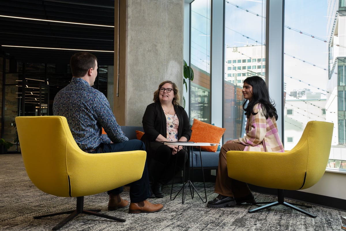 Colleagues chatting in a bright office lounge with yellow armchairs
