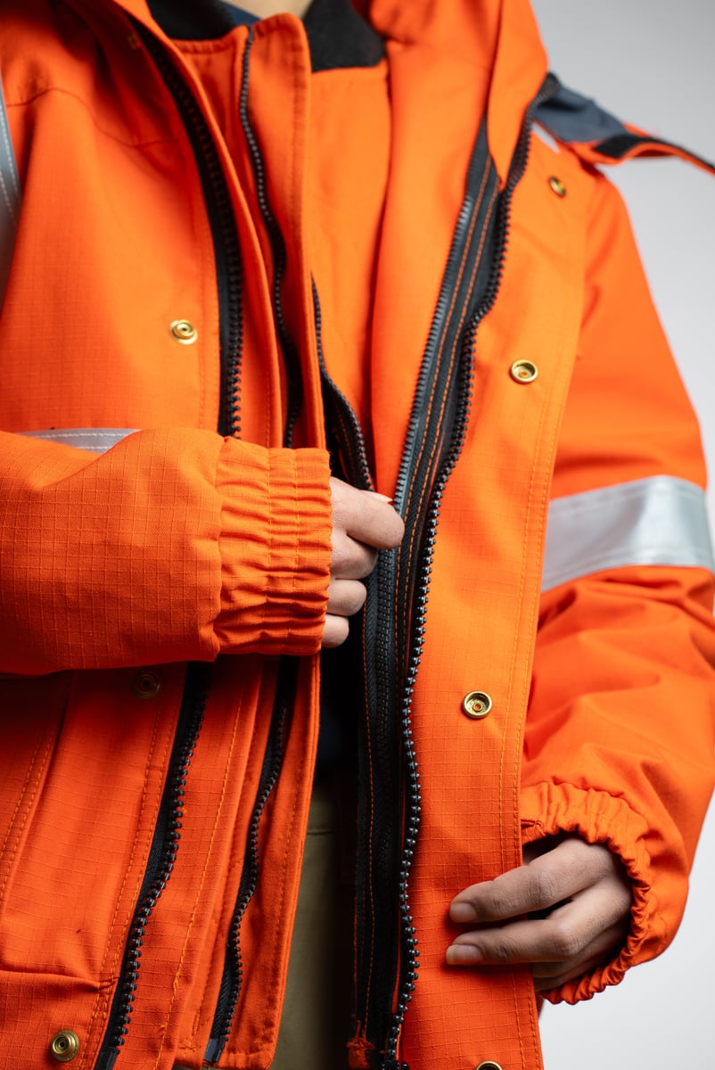 Close-up product photography of the pocket and storm flap on an orange work jacket