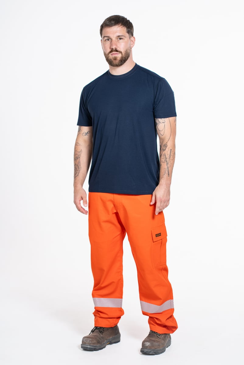 Full-length e-commerce photo of a model in navy tee and orange hi-vis work pants